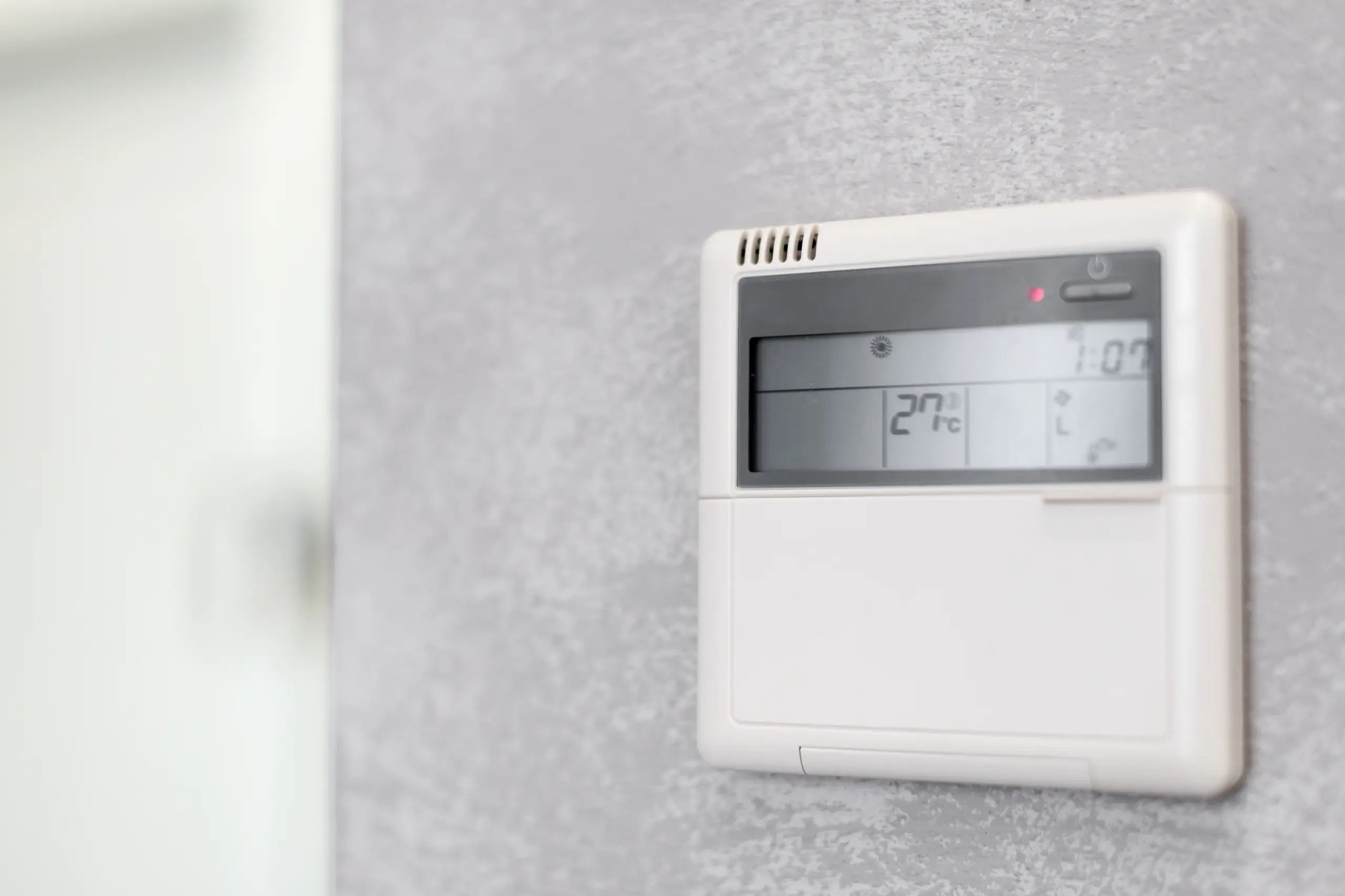 Cyfrowy termostat ścienny systemu HVAC wyświetlający 27°C